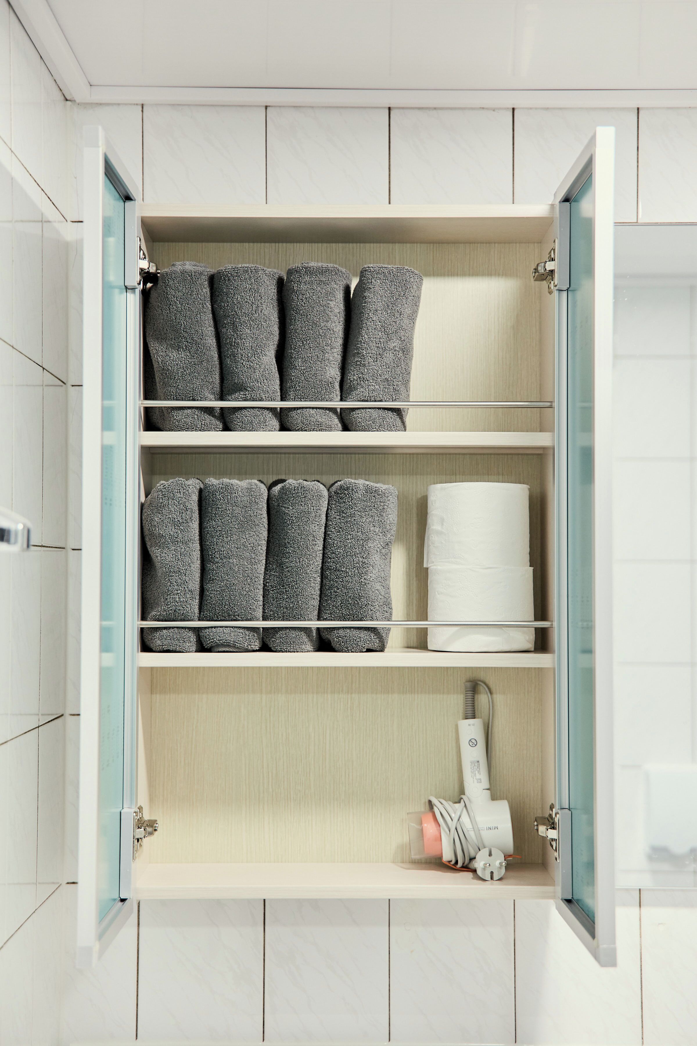 Un baño con pared de azulejos blancos, tocador de madera y un perchero con toallas dobladas.