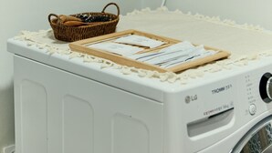 Ein Waschbereich mit einer weißen Waschmaschine, einem Korbwäscheschrank und einem gerahmten Kunstwerk an der Wand.