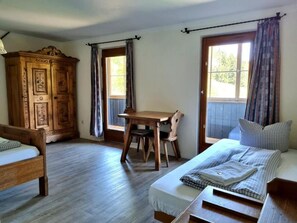 A room with two wooden beds, a wooden wardrobe, a small wooden table, and a window with curtains. - Berggasthof Almagmach (Immenstadt im Allgaeu)