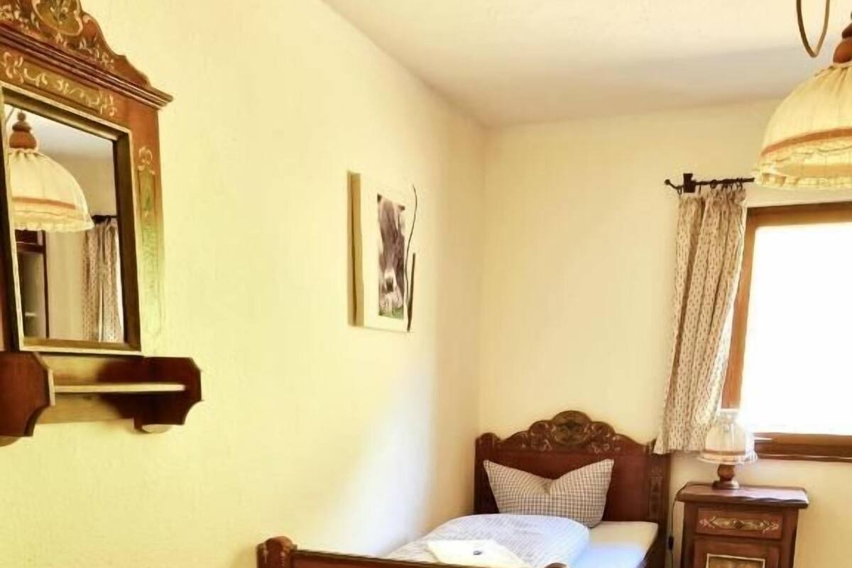 Ein Schlafzimmer mit einem hölzernen Bett, einem Nachttisch, einem Spiegel und einem Fenster mit Vorhängen.