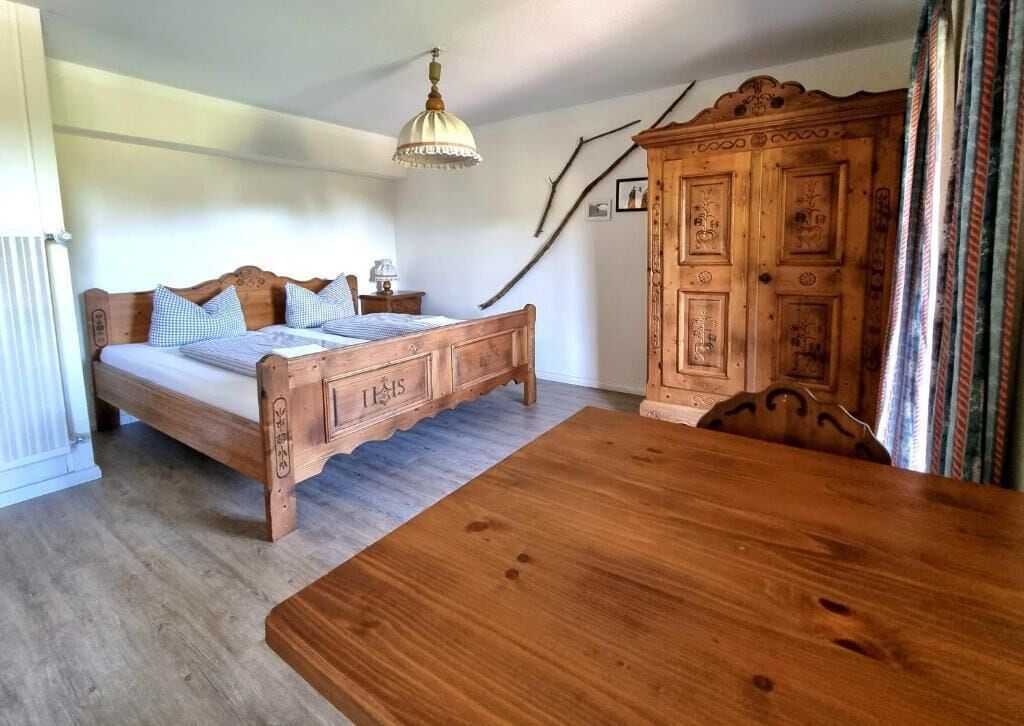 A bedroom with a wooden bed, a wooden table, a wardrobe, and a hanging lamp.