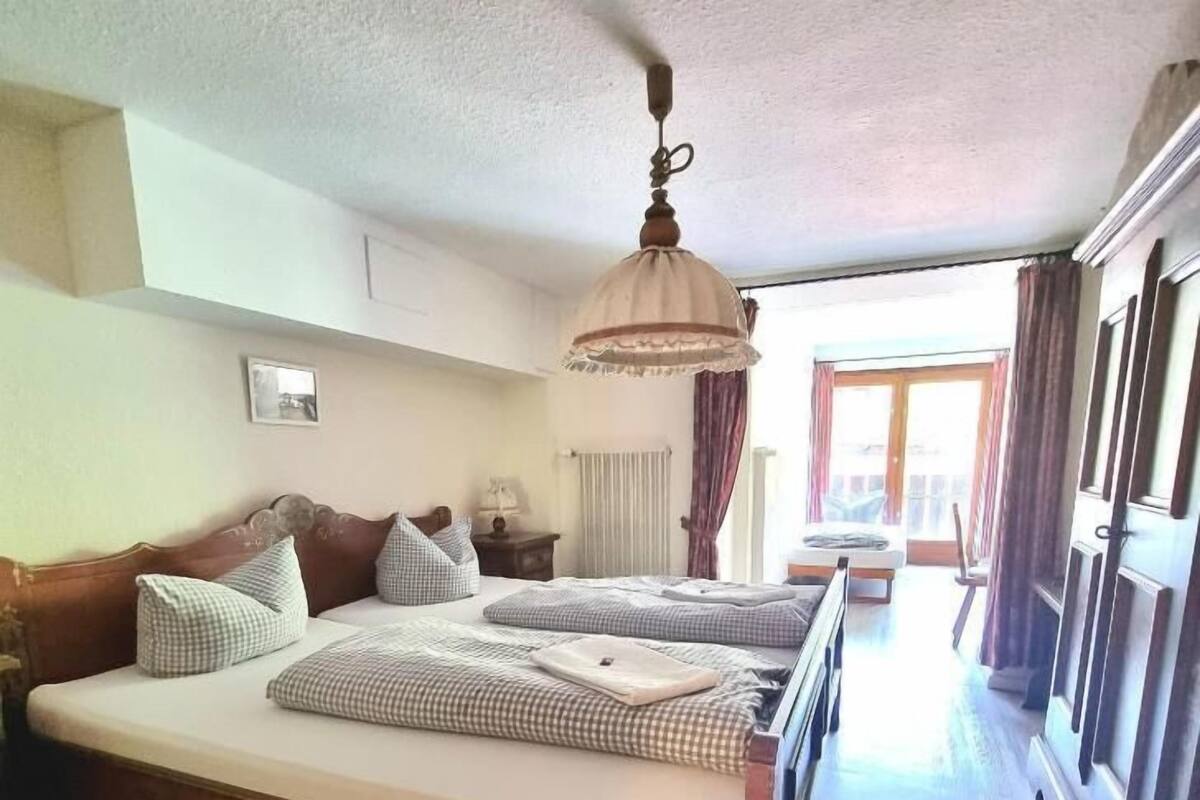 Ein Hotelzimmer mit einem großen Bett, einem Nachttisch, einer Lampe, einem Fenster mit Vorhängen und Blick ins Freie.
