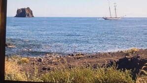 A coastal scene with a rocky shoreline, a small island, and a sailing ship in the distance. - Ada Stromboli House in Piscità, close to the beach and the Cave of Aeolus. (Stromboli)