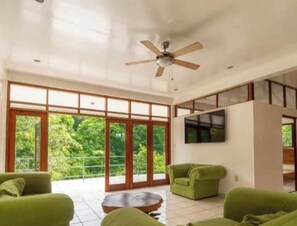 A spacious living area with large sliding glass doors, a ceiling fan, and green sofas. - Crown Jewel Eco Villa (San Ignacio)