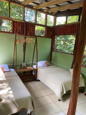 A room with two beds, a hanging chair, and a view of greenery through the windows. - Crown Jewel Eco Villa (San Ignacio)