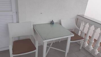 A small outdoor seating area with a table and two chairs, a white railing, and a plain wall.