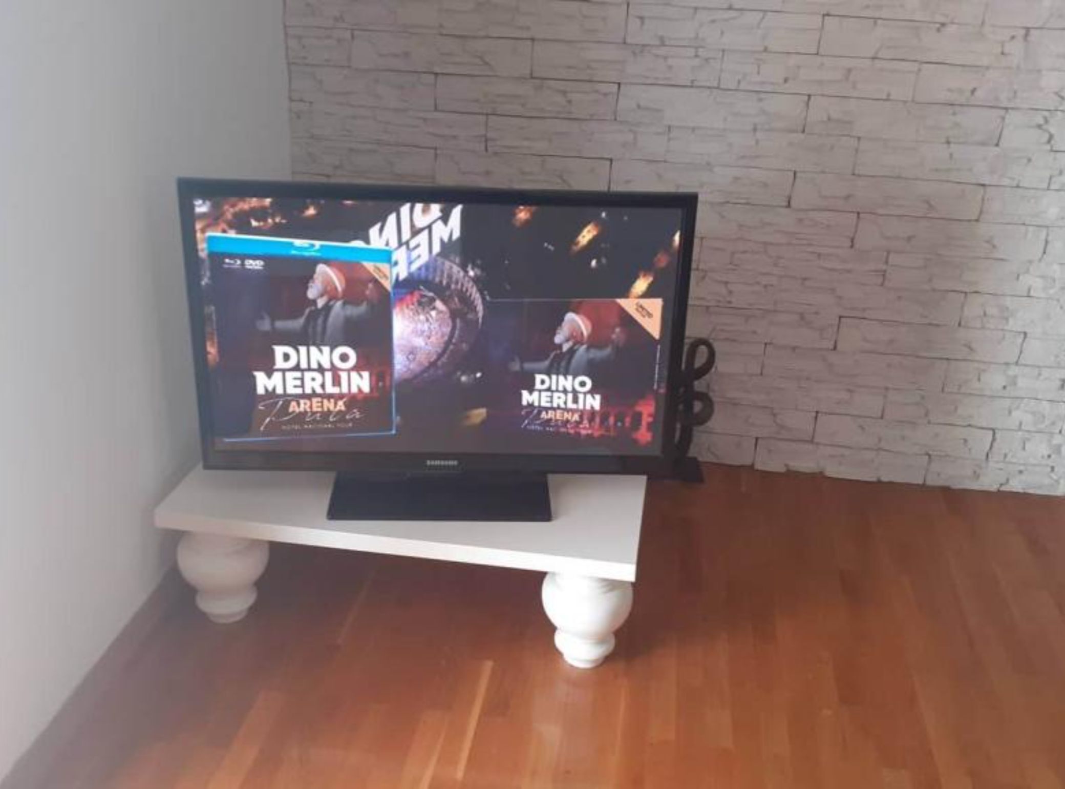 Un téléviseur posé sur un meuble blanc, avec un mur en briques en arrière-plan.