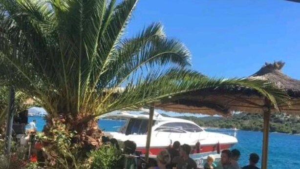 A boat docked near a coastal area with a thatched roof structure and palm trees. - Villa Ivan Vodice (Vodice)