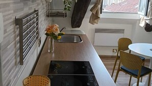 Et kompakt køkken med komfur, vask og et lille spiseområde med to stole.