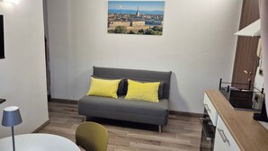 Et moderne værelse med en grå sofa, gule puder, et fladskærms-TV, et spisebord med stole og udsigt over bybilledet.