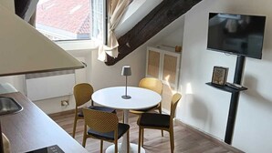 Et moderne køkken med indbygget komfur, et spiseområde med et rundt bord og stole, et TV monteret på væggen og et vindue med gardiner.
