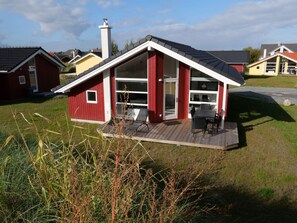 A red house with a large glass door, a deck with chairs, and a chimney. - 4 Star Holiday Home in Grossenbrode (Grossenbrode)