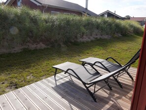 A deck with two lounge chairs, a grassy area, and a red building in the background. - 4 Star Holiday Home in Grossenbrode (Grossenbrode)