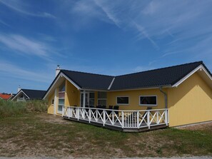 A yellow building with a black roof, a white porch, and a clear blue sky. - Coastal Base With Sauna, Sun Deck (Grossenbrode)