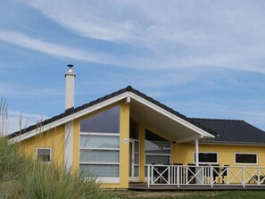 A yellow building with a white roof, a chimney, and a balcony with white railings. - Coastal Base With Sauna, Sun Deck (Grossenbrode)