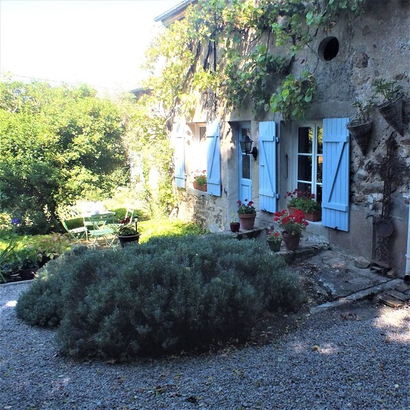 A rustic stone building with blue shutters, a gravel driveway, and potted plants.