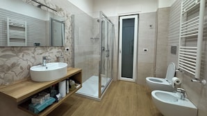 Een moderne badkamer met een douchecabine van glas, twee wasbakken, een toilet en een wastafelmeubel met opbergruimte.