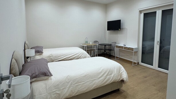 Een moderne slaapkamer met twee bedden, een bureau, een televisie en een raam met jaloezieën.