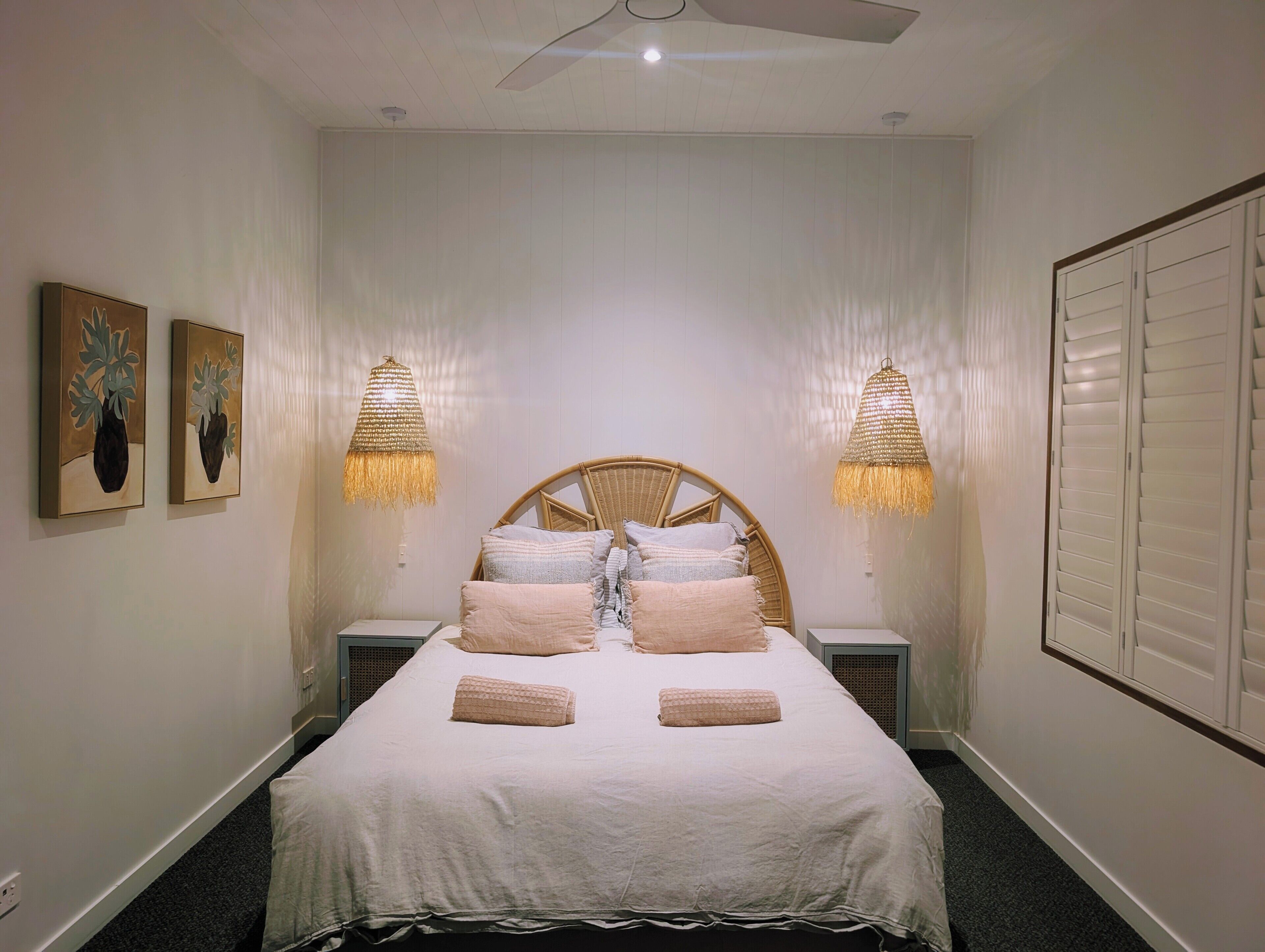 Une chambre à coucher avec un lit, deux lampes fixées au mur et deux œuvres d’art encadrées.
