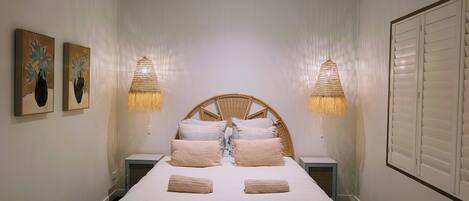 Une chambre à coucher avec un lit, deux lampes fixées au mur et deux œuvres d’art encadrées.