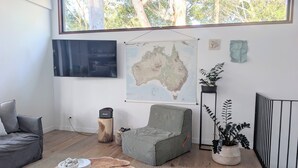 Ett vardagsrum med ett stort fönster, en platt-TV, en karta över Australien, en grå soffa, ett runt soffbord och en krukväxt.