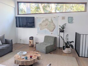 Un salon doté d’une grande fenêtre, d’un téléviseur à écran plat, d’une carte de l’Australie, d’un canapé gris, d’une table basse ronde et d’une plante en pot.
