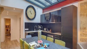 Une cuisine moderne avec une grande horloge murale, une table à manger avec des chaises et une lucarne au-dessus.