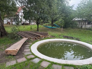 Un jardín con un estanque, escalones de madera, una hamaca y un edificio con fachada blanca.
