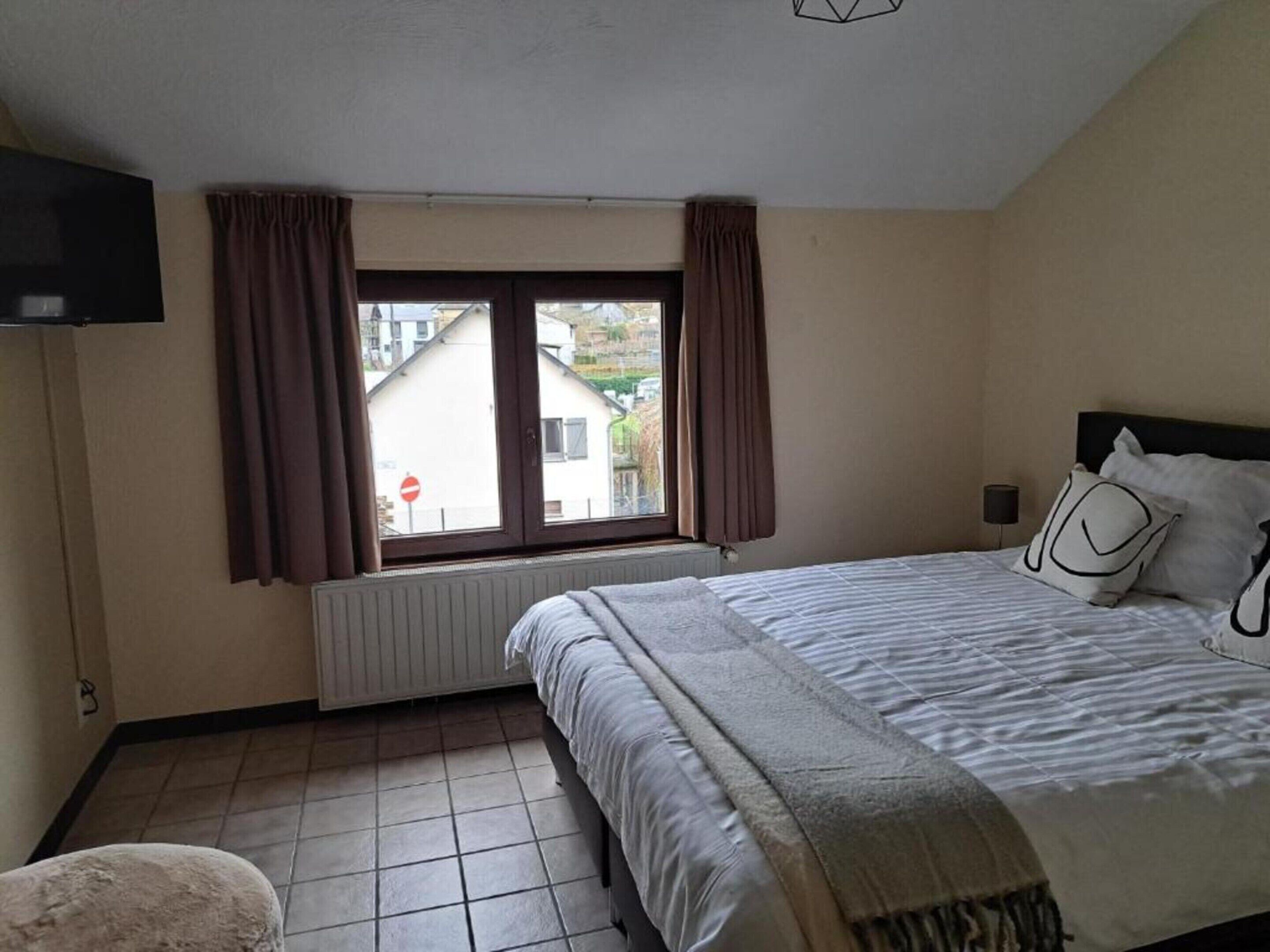 Une chambre à coucher avec un lit, une fenêtre avec des rideaux, un radiateur et un téléviseur fixé au mur.