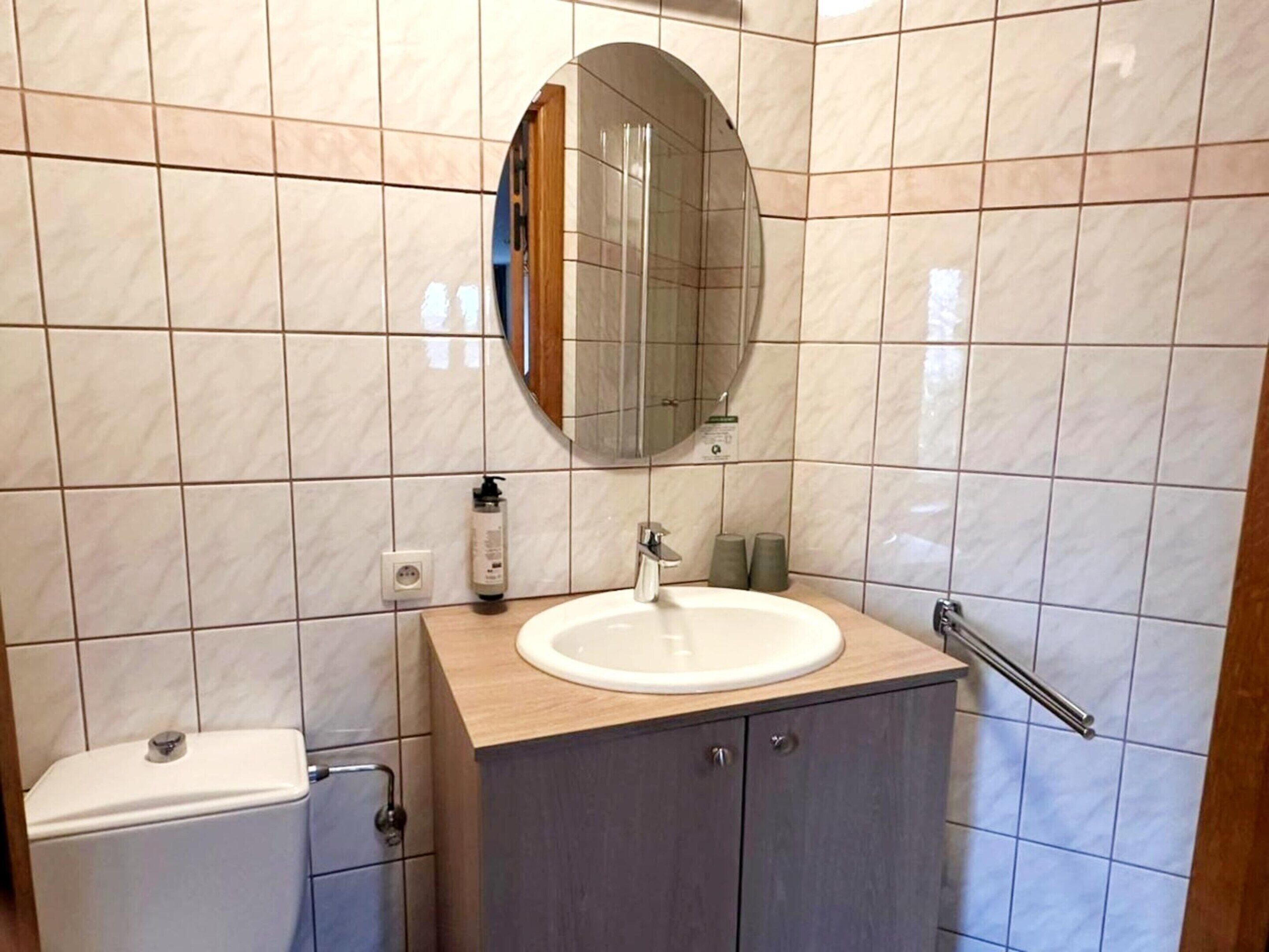 Een badkamer met toilet, wastafel, spiegel en betegelde wanden.