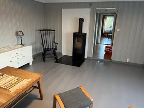A living room with a fireplace, a wooden table, a chair, and a white dresser. - Charming and idyllic Westland house (Vestland)