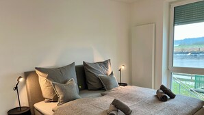 Ein Schlafzimmer mit Bett, Kissen, Decke, einer Lampe und Blick auf ein Gewässer.