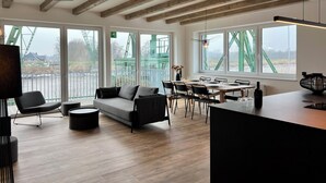 Ein modernes Interieur mit Holzbalkendecke, großen Fenstern, einer Couch, einem Esstisch und Stühlen.