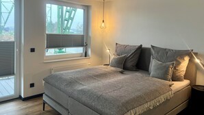 Une chambre moderne avec un lit, une fenêtre équipée de stores, un luminaire suspendu et un radiateur.