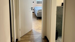Un couloir au plancher de bois menant à une chambre à coucher équipée d’un lit et d’une fenêtre.