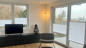 Un salon moderne avec un téléviseur à écran plat, un canapé gris, une table basse ronde et une lampe noire.
