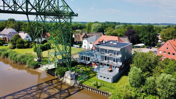 Un bâtiment situé au bord de la rivière, doté d’un balcon, d’un pont et entouré de verdure.