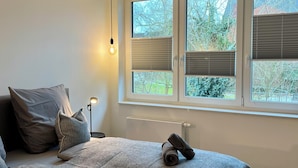 A bedroom with a bed, pillows, a lamp, a window with blinds, and a radiator. - Apartment house „Osten – An der Schwebefähre“ – Apartment 4 (Osten)