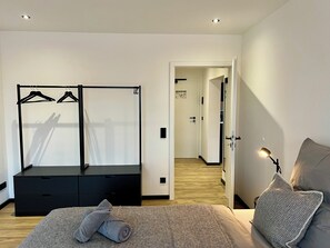 Een slaapkamer met een bed, een kledingkast, een zwevend kastje en een gang naar een andere kamer.