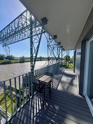 A balcony with a view of a river, a metal bridge, and a grassy area. - Apartment house „Osten – An der Schwebefähre“ – Apartment 7 (Osten)