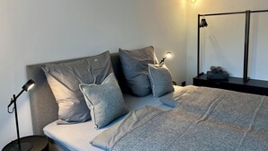 Una camera da letto ordinata con un letto, cuscini, una lampada da comodino, uno specchio e un piccolo tavolo con asciugamani.