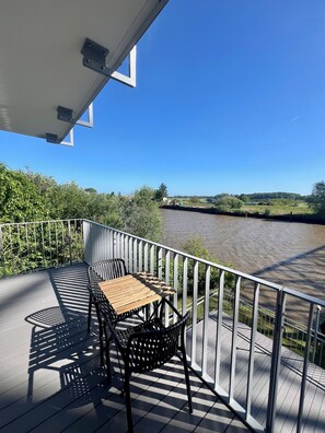 A balcony with a table and chairs, overlooking a river. - Apartment house „Osten – An der Schwebefähre“ – Apartment 8 (Osten)