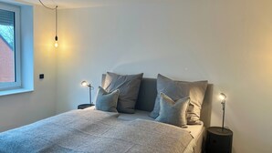 Ein modernes Schlafzimmer mit einem Bett, zwei Nachttischlampen, einem Fenster und einer Wandleuchte.