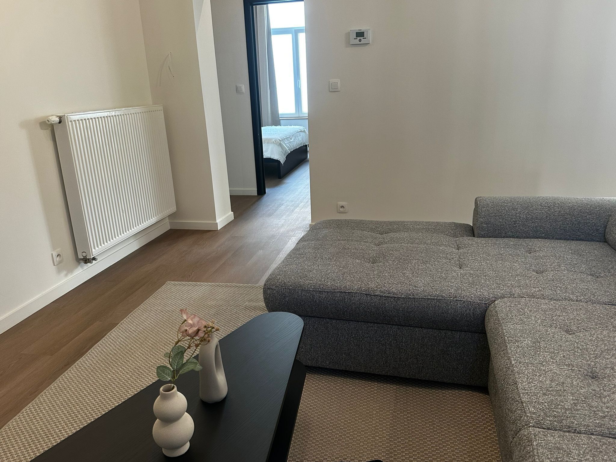 Ein modernes Wohnzimmer mit einem Ecksofa, einem schwarzen Couchtisch und einer Heizung.