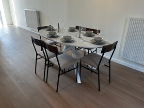 Uma mesa de jantar posta com pratos, tigelas e copos de vinho, rodeada por cadeiras.