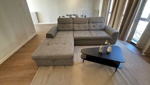 En moderne stue med en hjørnesofa, et sofabord og et spiseområde i baggrunden.