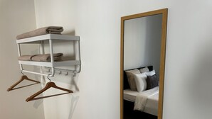 Et badeværelse med et hvidt håndklædestativ, et spejl med træramme og en seng med puder.