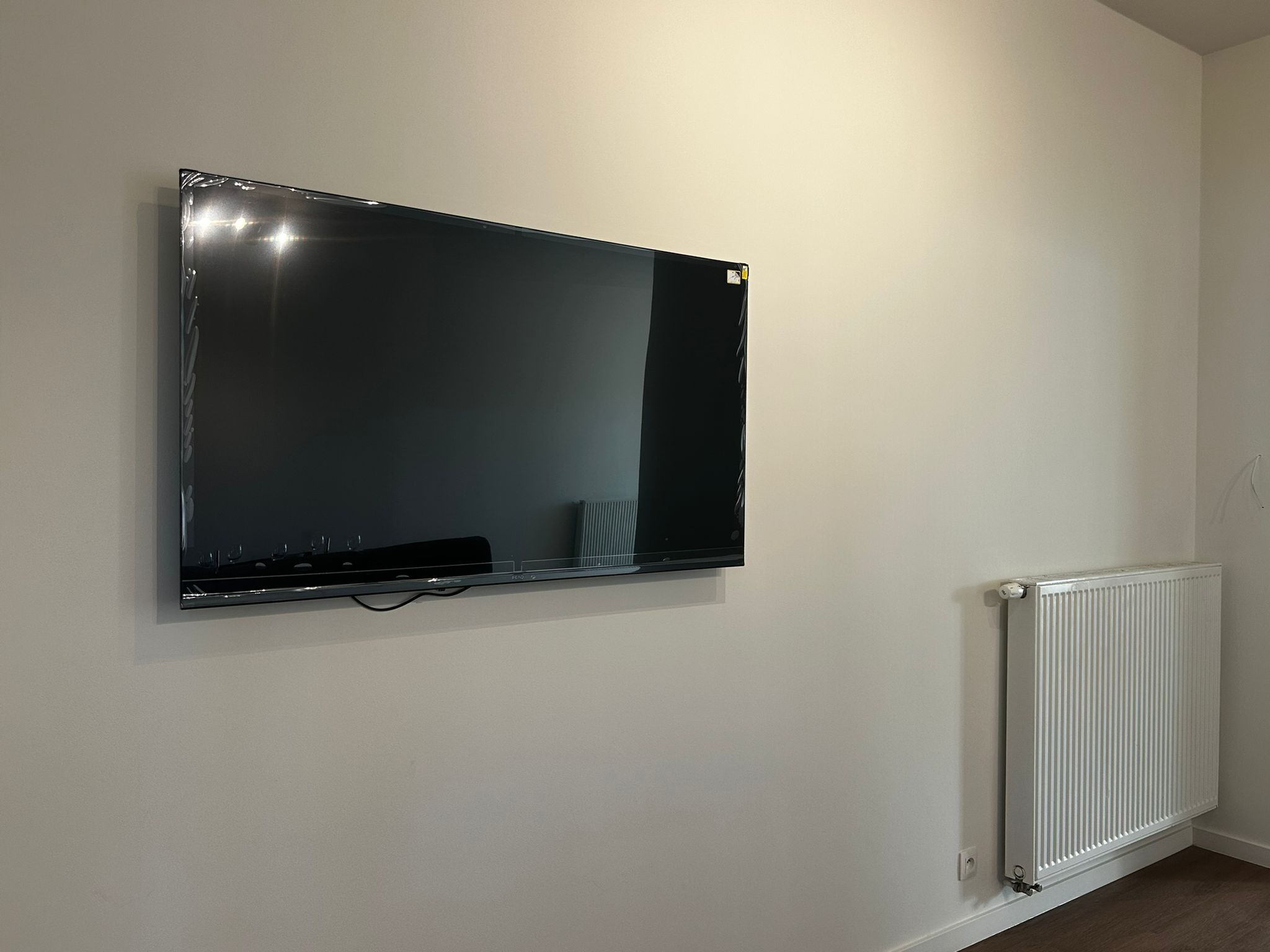 A wall-mounted flat-screen TV, a white radiator, and a plain wall.