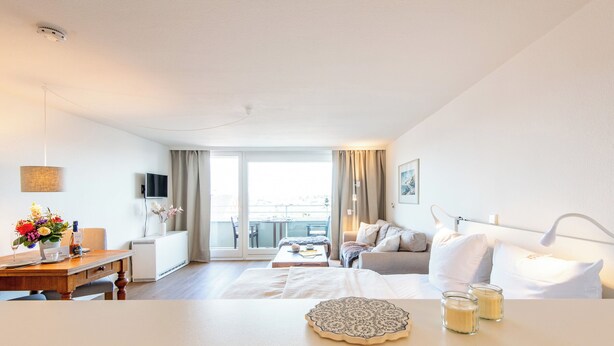 A hotel room with a bed, bedside table, a small desk with a chair, a TV, and a balcony with a view. - Hanseatenhaus Sea Nest 43 - Westerland (Westerland)