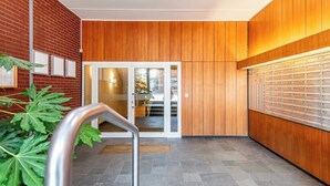 A modern lobby with a brick wall, wooden paneling, a glass door entrance, and a metal railing. - Hanseatenhaus Sea Nest 43 - Westerland (Westerland)